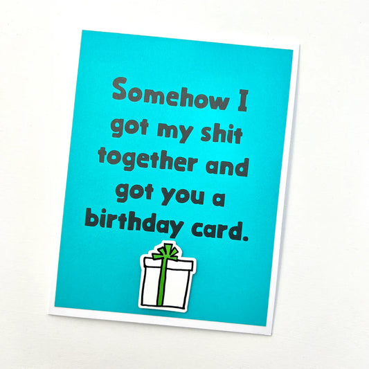 Blue birthday card with humorous text and a gift illustration on a white background